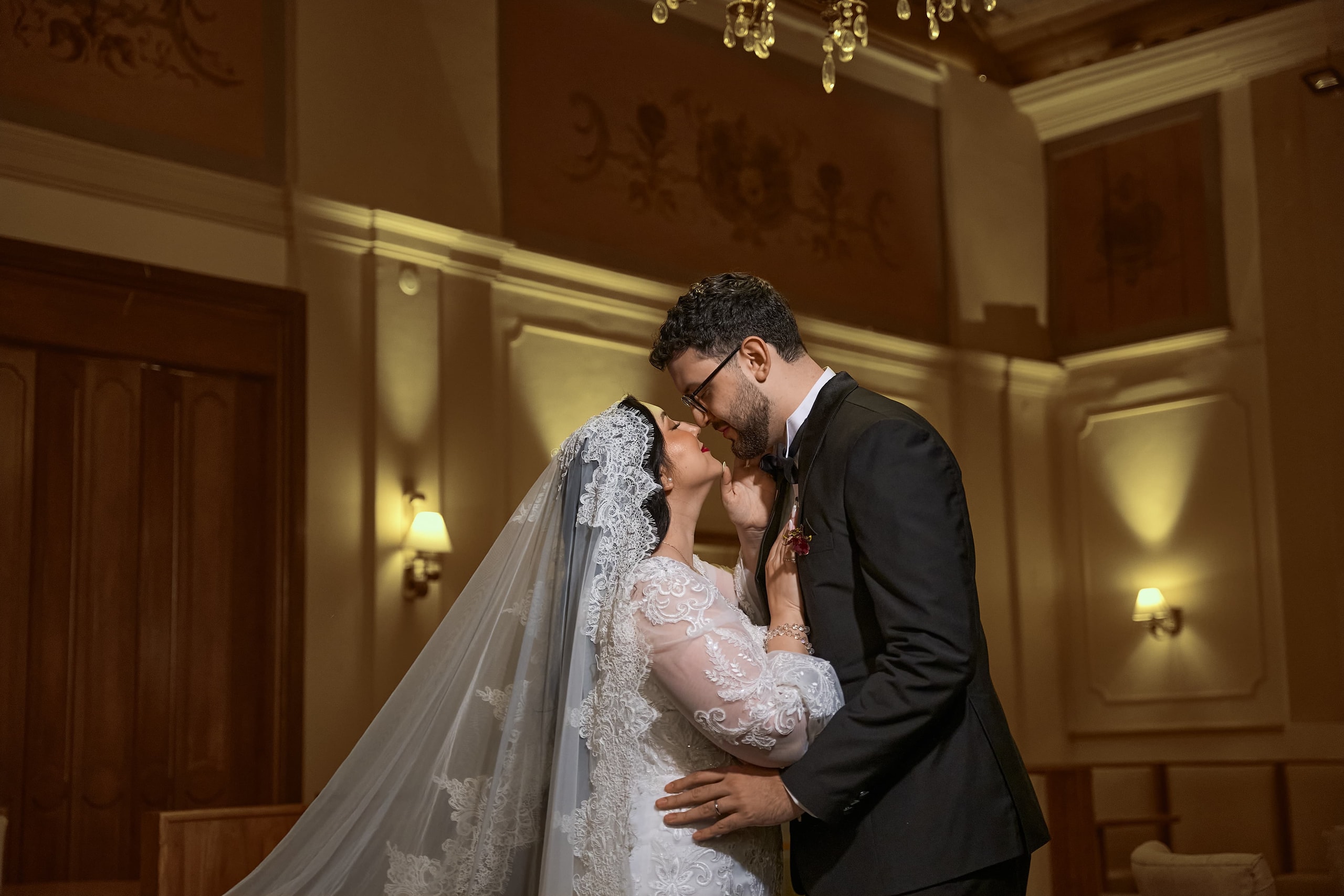Los novios a punto de besarse en un salón de molduras doradas, ella con mantilla de encaje y él de esmoquin
